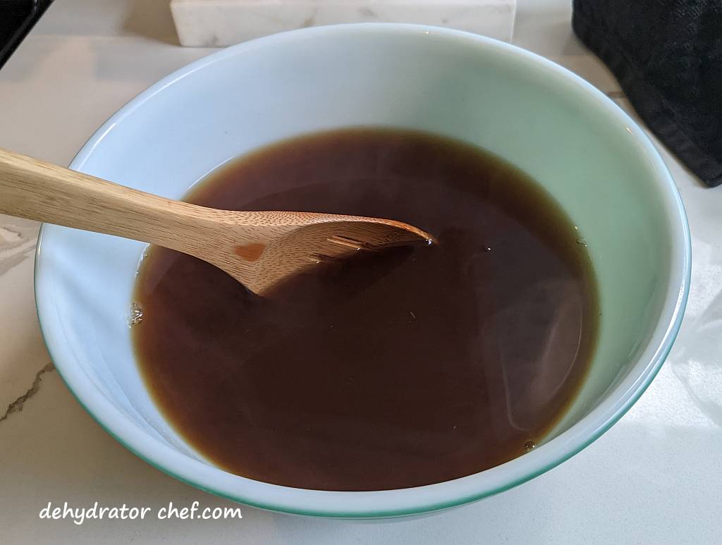 mixing hot beef stock and gelatin in a large bowl for our dehydrated beef stock project.