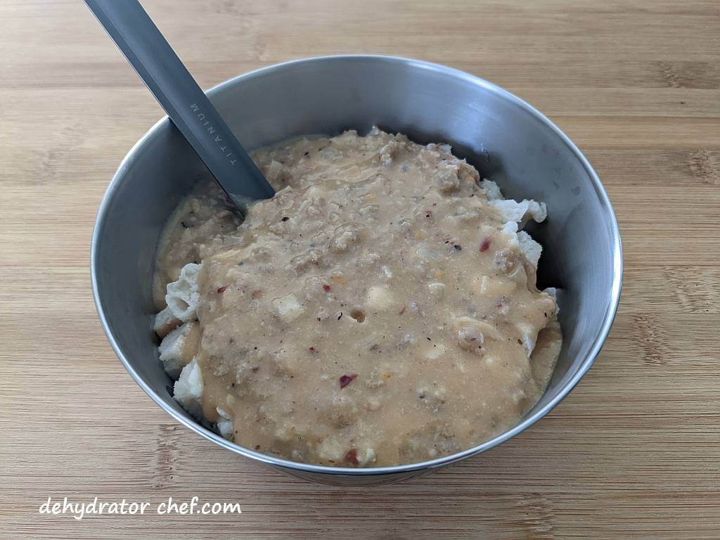 dehydrated biscuits and gravy in a stainless steel camping bowl with a long handle spoon | making dehydrated meals for camping | homemade dehydrated meal recipes | make your own dehydrated camping food | homemade dehydrated camping meals | homemade dehydrated backpacking meals