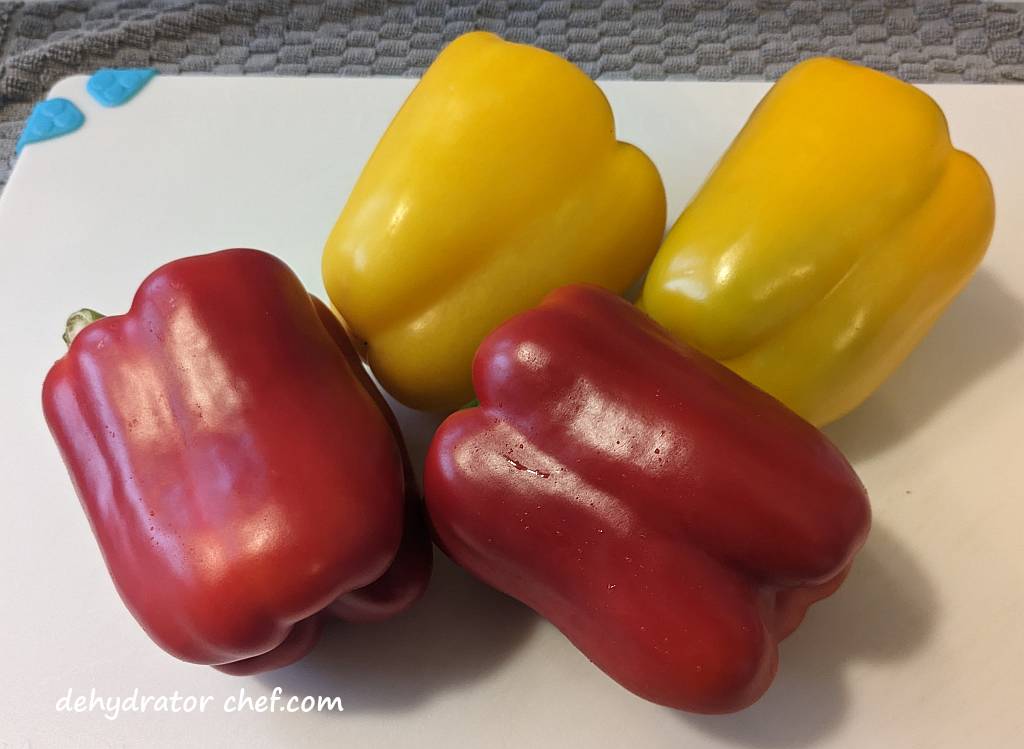 red and yellow peppers on a cutting board | | dehydrating bell peppers | how to dehydrate bell peppers | dehydrating green peppers | dehydrating red peppers | dehydrating yellow peppers | best foods to dehydrate for long term storage | dehydrating food for long term storage | dehydrated food recipes for long term storage | dehydrating meals for long term storage | food dehydrator for long term storage