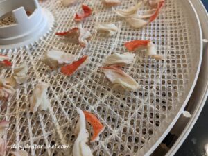 a close up of dehydrated crab meat on a dehydrator tray | dehydrated imitation crab meat | dehydrating imitation crab meat | how to dehydrate imitation crab meat | best foods to dehydrate for long term storage | dehydrating food for long term storage | dehydrated food recipes for long term storage | dehydrating meals for long term storage | food dehydrator for long term storage | making dehydrated meals for camping | homemade dehydrated meal recipes | make your own dehydrated camping food | homemade dehydrated camping meals | homemade dehydrated backpacking meals