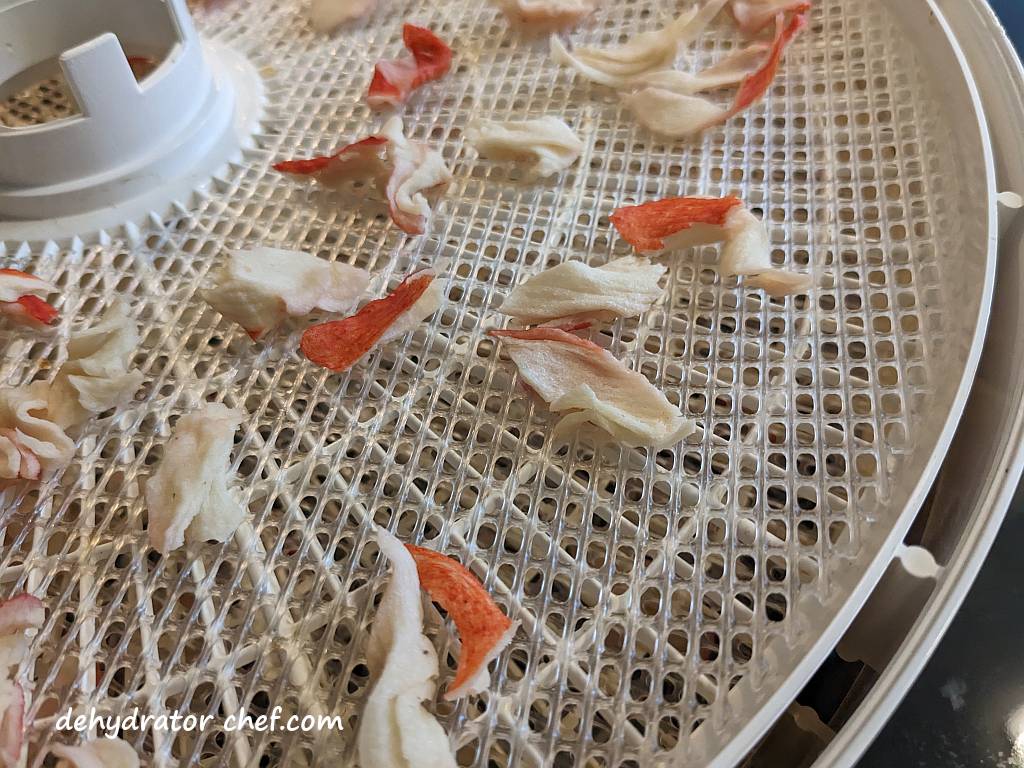 a close up of dehydrated crab meat on a dehydrator tray | dehydrated imitation crab meat | dehydrating imitation crab meat | how to dehydrate imitation crab meat | best foods to dehydrate for long term storage | dehydrating food for long term storage | dehydrated food recipes for long term storage | dehydrating meals for long term storage | food dehydrator for long term storage | making dehydrated meals for camping | homemade dehydrated meal recipes | make your own dehydrated camping food | homemade dehydrated camping meals | homemade dehydrated backpacking meals