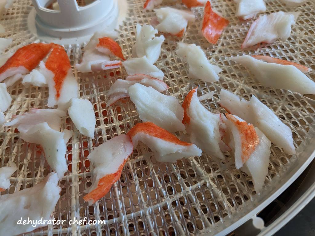 close up of imitation crab meat on a dehydrator tray | dehydrated imitation crab meat | dehydrating imitation crab meat | how to dehydrate imitation crab meat | best foods to dehydrate for long term storage | dehydrating food for long term storage | dehydrated food recipes for long term storage | dehydrating meals for long term storage | food dehydrator for long term storage | making dehydrated meals for camping | homemade dehydrated meal recipes | make your own dehydrated camping food | homemade dehydrated camping meals | homemade dehydrated backpacking meals