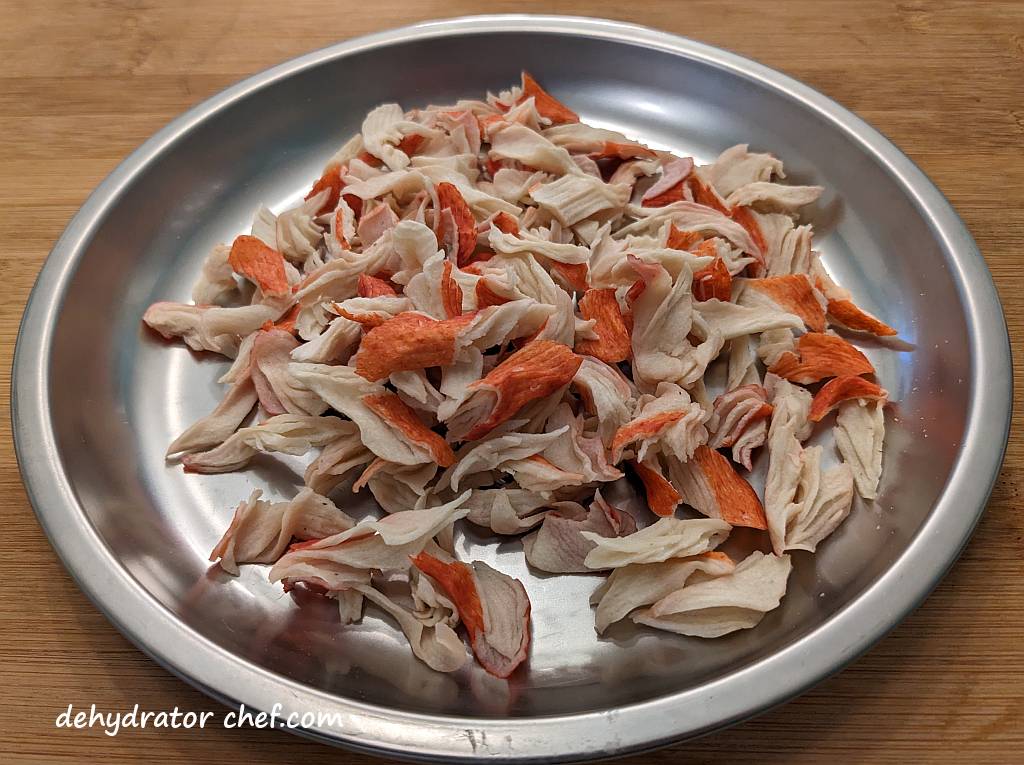 Dehydrated imitation crab meat on a metal camping plate. | dehydrated imitation crab meat | dehydrating imitation crab meat | how to dehydrate imitation crab meat | best foods to dehydrate for long term storage | dehydrating food for long term storage | dehydrated food recipes for long term storage | dehydrating meals for long term storage | food dehydrator for long term storage | making dehydrated meals for camping | homemade dehydrated meal recipes | make your own dehydrated camping food | homemade dehydrated camping meals | homemade dehydrated backpacking meals