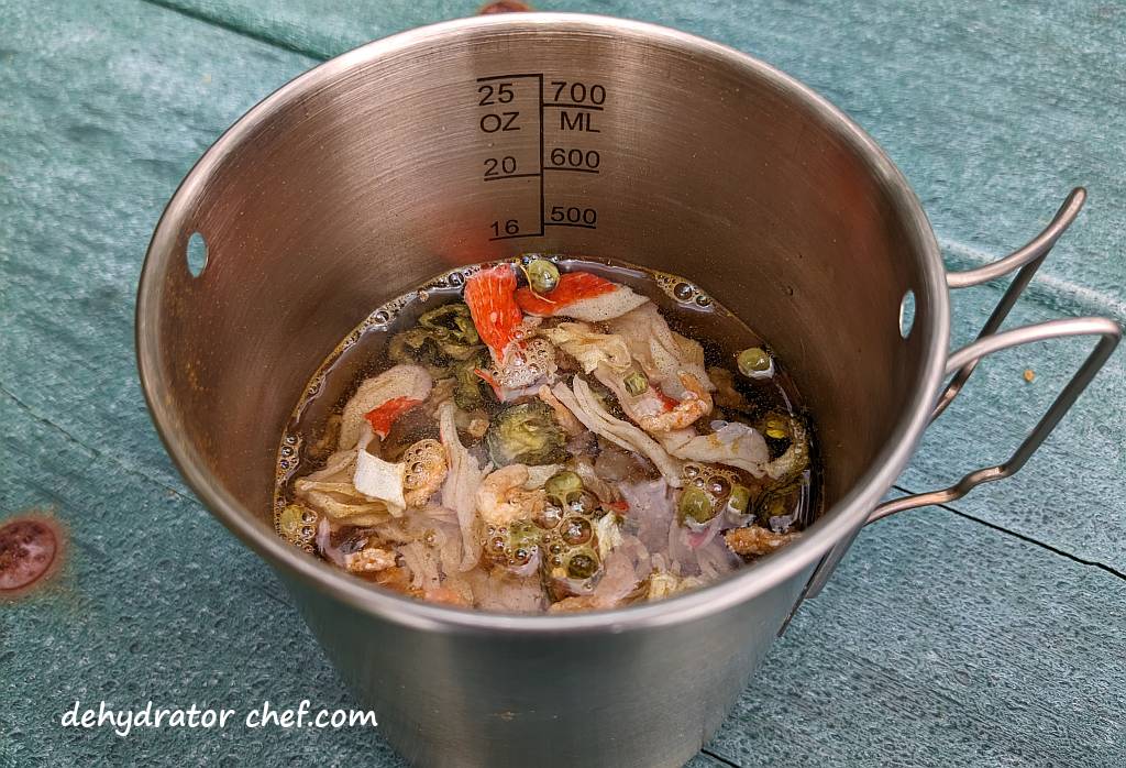 Shown is the stainless-steel camping mug that we poured in enough water to cover the dry mix. Then we added a tad bit more water.  Next, we will give everything a good stir, then let stand and rehydrate for at least five minutes.  We'll stir it every minute or so to keep everything well saturated with water.   Add more water if needed. | Adding water to the seafood curry dry mix. | Dehydrated seafood curry. | Making dehydrated meals for camping. | Homemade dehydrated meal recipes. | How to make your own dehydrated camping food. | Homemade dehydrated camping meals. | Homemade dehydrated backpacking meals.