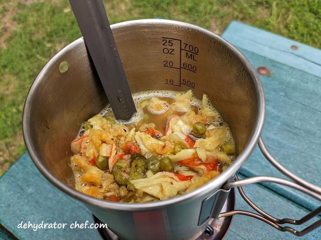 Shown is the cooking seafood curry, which absorbed quite a bit of water and we need to add a tad bit more. We’ll monitor it closely during the brief 2-minute boil and simmer.  Frequent stirring is crucial in avoiding burnt, stuck-on food. |  Dehydrated seafood curry. | Making dehydrated meals for camping. | Homemade dehydrated meal recipes. | How to make your own dehydrated camping food. | Homemade dehydrated camping meals. | Homemade dehydrated backpacking meals.