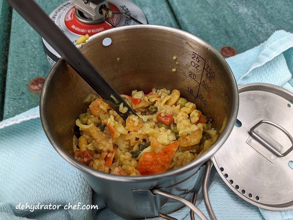 Shown is our reconstituted seafood curry is ready to eat. Can you smell that? It smells good! This is one really delicious homemade dehydrated camping meal recipe. You can see pieces of shrimp, crab, rice, peas, and carrots, all coated in a spicy, warm, and flavorful curry sauce. | The dehydrated seafood curry MRE has been reconstituted and we are ready to eat. | Dehydrated seafood curry | Making dehydrated meals for camping. | Homemade dehydrated meal recipes. | How to make your own dehydrated camping food. | Homemade dehydrated camping meals. | Homemade dehydrated backpacking meals.