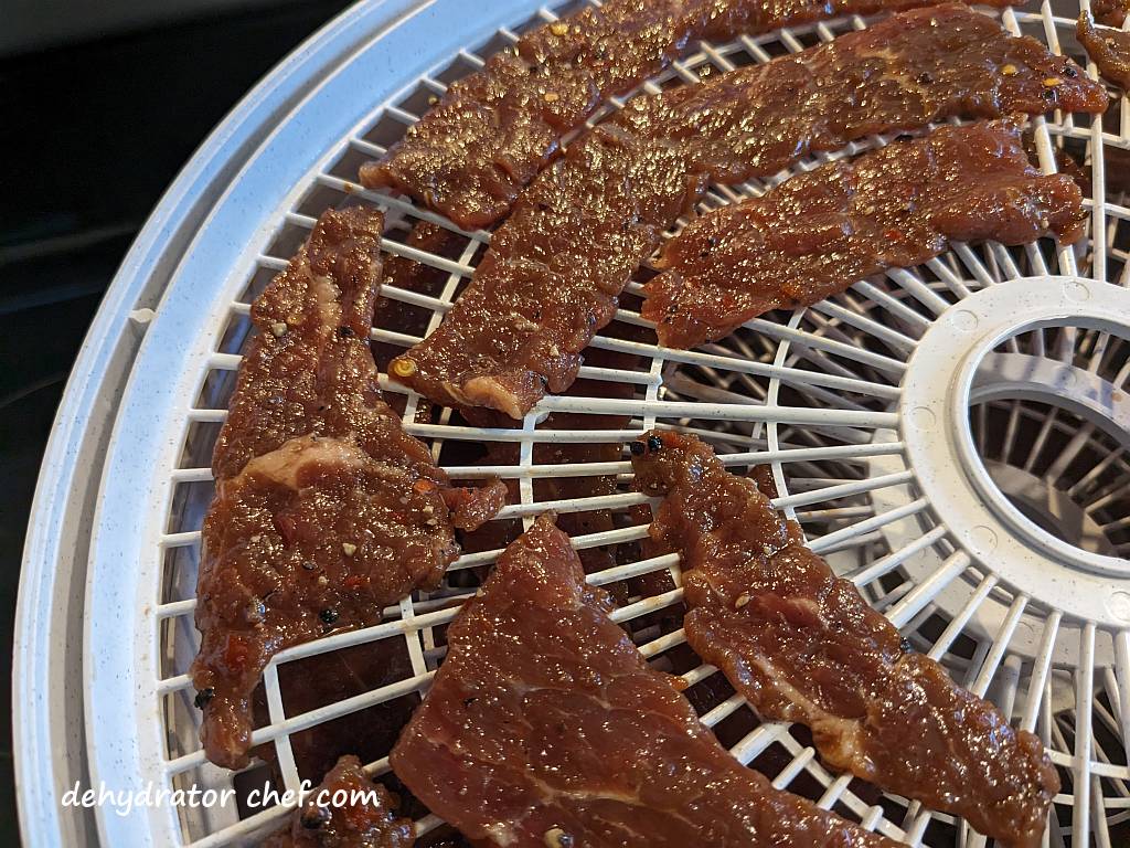 close up of beef jerky on a food dehydrator tray | how to make beef jerky | best foods to dehydrate for long term storage | dehydrating food for long term storage | dehydrated food recipes for long term storage | dehydrating meals for long term storage | food dehydrator for long term storage