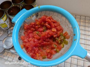 Draining the excess canning liquid using a mesh strainer from these diced tomatoes that we will dehydrate and use in our homemade dehydrated camping meals and to stock up the pantry. Dehydrated diced tomatoes are among the best foods to dehydrate for long-term storage because they are used in so many of our recipes.