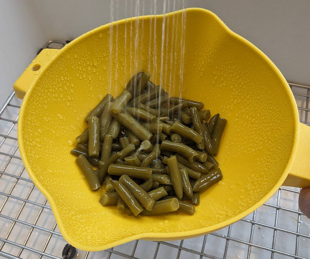 We're draining and rinsing away the salty canning liquid and inspecting the green beans for anything we wouldn't want to eat, such as woody stem pieces.