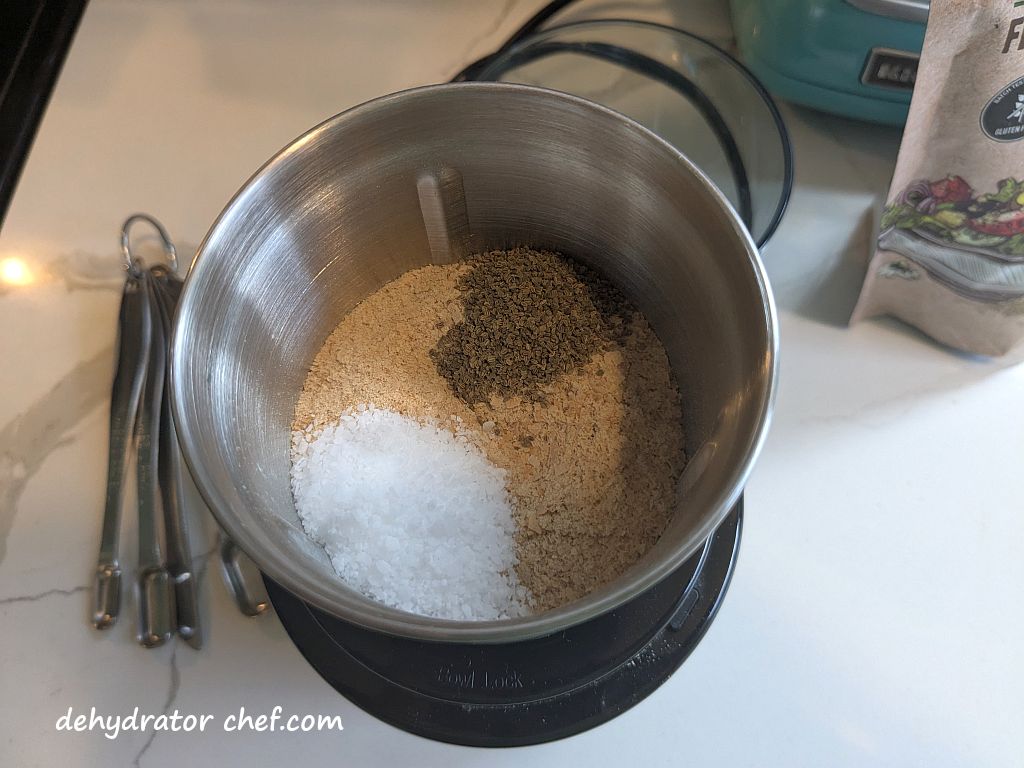 The nutritional yeast flakes, celery seed, and kosher salt in the spice grinder bowl.