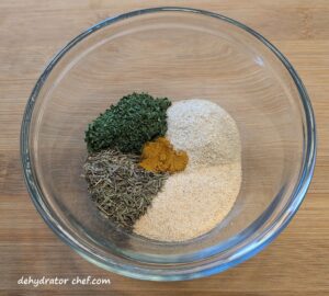 The homemade vegetable bouillon step 2 ingredients in a small bowl. From the top left going clockwise; dehydrated parsley, onion powder, garlic powder, thyme. In the center is turmeric.