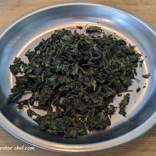 Here is a plate full of dehydrated spinach, a multipurpose staple for our dehydrated meals for camping or homemade dehydrated backpacking meals. Lightweight and shelf-stable, we can store it for long-term use knowing it will keep for up to a year or more with proper storage.