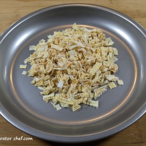 Dehydrated onions on a plate, ready for long-term storage and use in homemade backpacking meals.