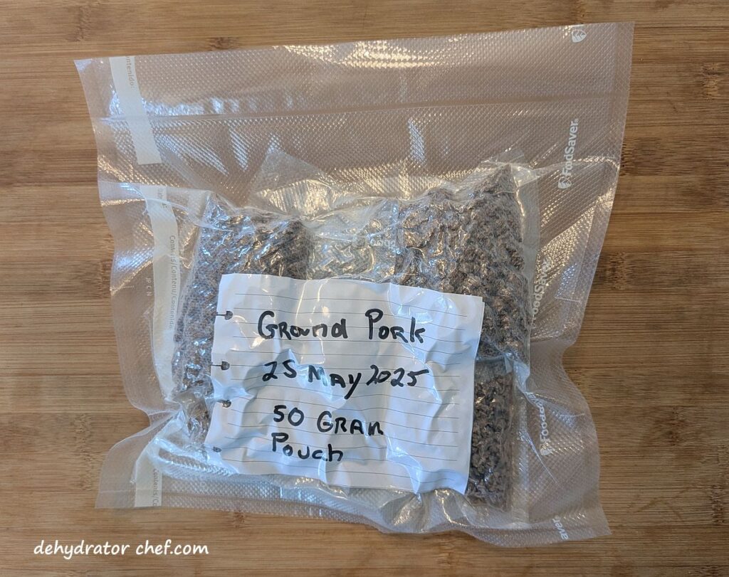We placed all of the 50-gram single-serving vacuum-sealed packets of dehydrated ground pork crumbles into a larger vacuum-sealed bag. We’re going to put this all into our freezer for long-term storage. When we want to make a few homemade camping meals, all we need to do is open the bag, grab what we need, then vacuum and seal the bag before returning it to the freezer. We’ll set the single-serving packets of pork crumbles on the counter to naturally warm up and thaw; they’re ready to go.