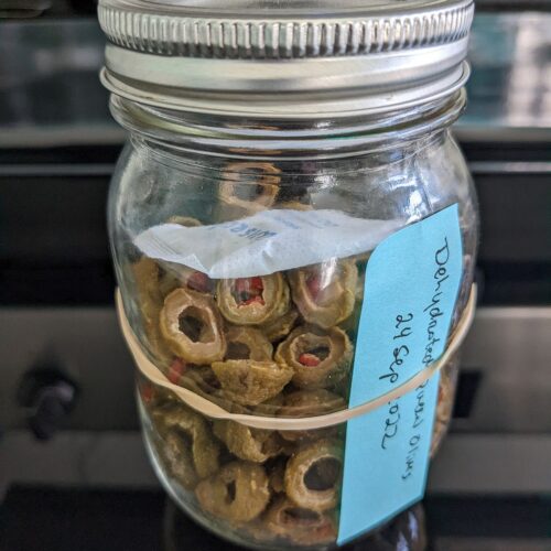 Dehydrated olive in a clear canning jar with a desiccant for moisture control, and ready for long-term storage, and also to use in homemade backpacking meals.