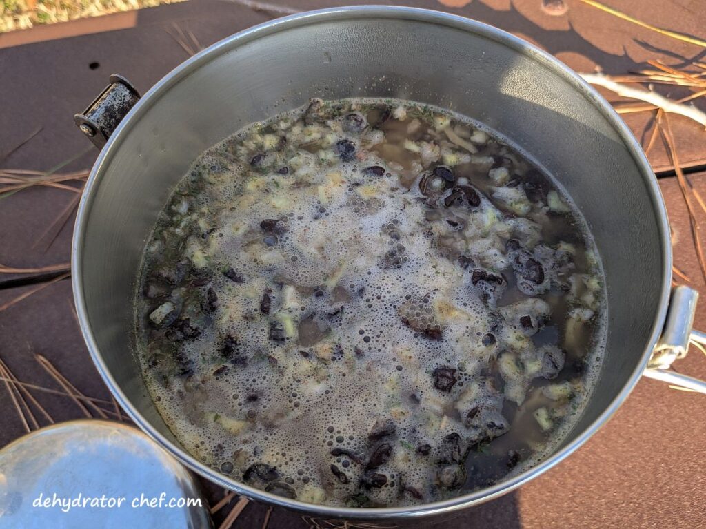 The black beans and rice are coming to a boil on the camp stove. The next step is to turn down the heat and simmer with the lid on the cooking pot for another 2 minutes.